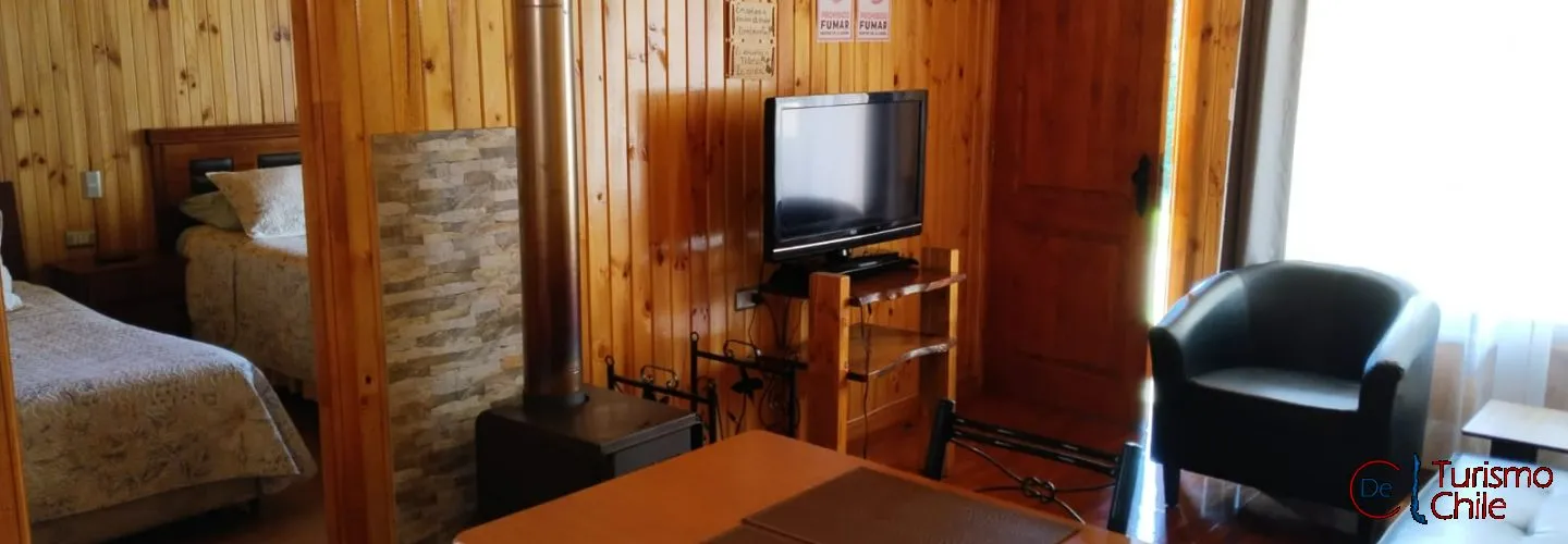 Interior cabaña Fabi con living, estufa a leña, TV y comedor en ambiente de madera